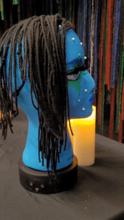 A blue styrofoam head with yarn hair and make-up spins on a table.